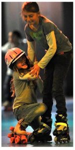 Older girl helping younger girl in helmet learn to skate
