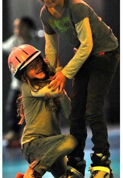 Older girl helping younger girl in helmet learn to skate