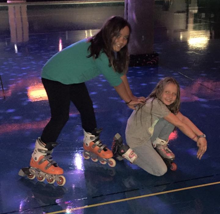 Happy sisters at skating rink wearing roller blades