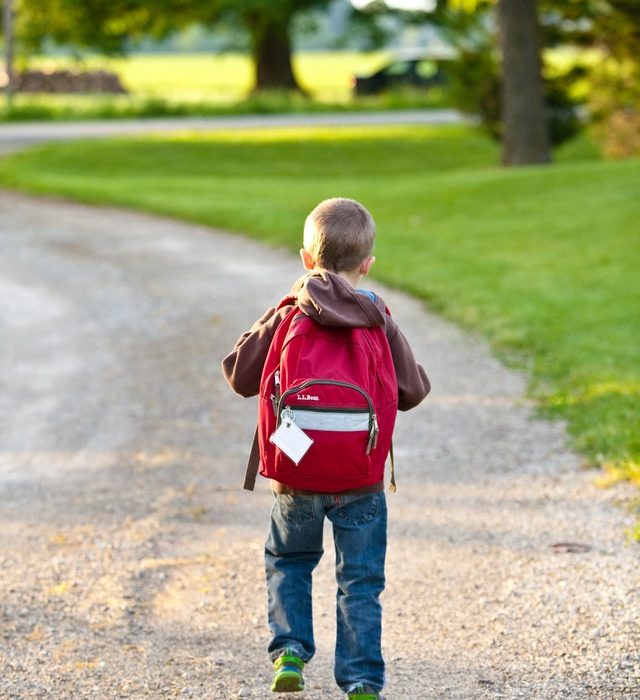 Small boy with red backpack walking down driveway for school