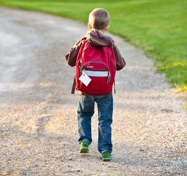 Small boy with red backpack walking down driveway for school