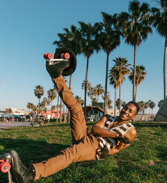 Man in roller skates and gloves laying on grass with foot in air