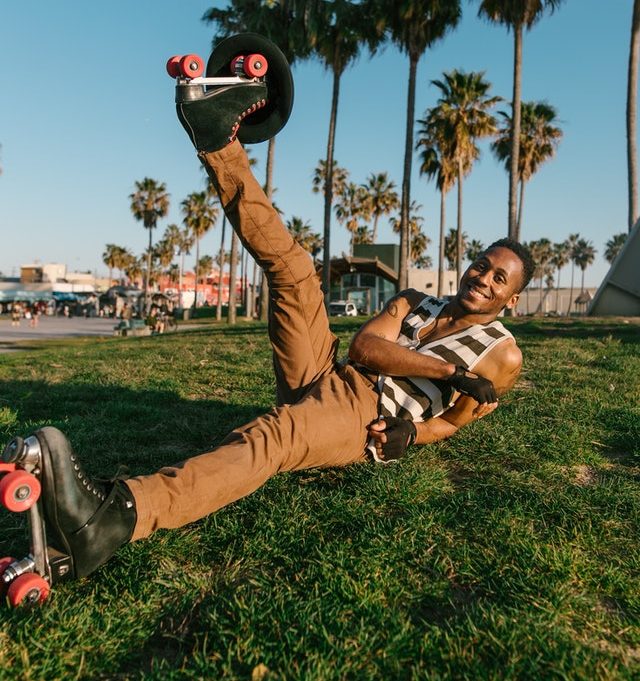 Man in roller skates and gloves laying on grass with foot in air