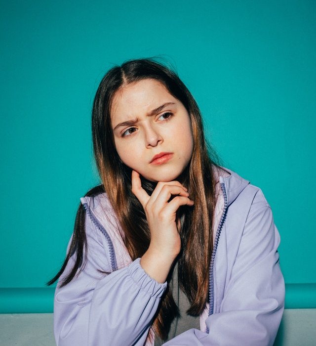 Girl in purple jacket touching chin and thinking with furrowed brow